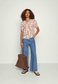Blusa de padrão vermelho e branco com mangas curtas, decote redondo, combinada com jeans flare azuis e uma bolsa de palha castanha. Sandálias baixas.