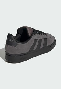 Szare zamszowe sneakersy z czarnymi skórzanymi akcentami, z trzema paskami na cholewce, okrągłym noskiem i teksturowaną gumową podeszwą. Logo na pięcie i boku.