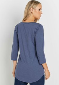 Dunkelblaues Langarmshirt mit abgerundetem Saum, weicher Textur und leicht lockerer Passform, getragen mit dunklen Jeans.