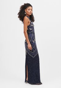 Námořnická beaded šaty s jemnými vzory, vysokým výstřihem a rozparkem; zdobené modrými a stříbrnými ozdobami, přizpůsobený střih.