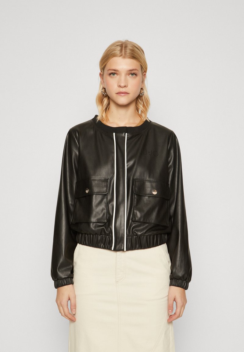 Giubbotto bomber in ecopelle nera con polsini elasticizzati, due tasche frontali e una cerniera bianca. Presenta un collo rotondo e un design cropped.