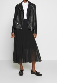 Svart läderbikerjacka med silverdetaljer, vit skjorta med krage, svart plisserad kjol och svarta platta skor med en dekorativ spänne.