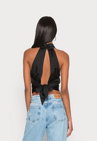 Černý saténový halter top s vázáním na zádech, hlubokým klíčovým výstřihem a hladkým povrchem; v kombinaci se světle modrými džínami s vysokým pasem.