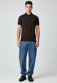 Dunkelbraunes Polohemd mit klassischem Kragen und dezentem Logo. Kombiniert mit hellblauen Jeans mit geradem Bein und schwarzen Schuhen. Minimalistisches Design.