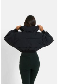 Chaqueta corta de plumón negra con cuello alto y puños acanalados, que presenta secciones cosidas y una textura suave.