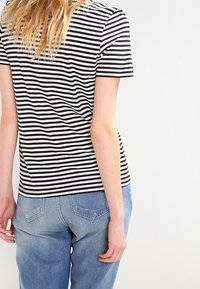 Czarna i biała bluzka w paski z krótkim rękawem i okrągłym dekoltem, wykonana z miękkiego materiału. W połączeniu ze jasnoniebieskimi dżinsami, prezentującymi luźny fason.