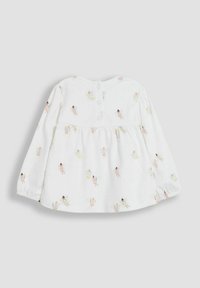 Hvid bluse med lange ærmer og samlet talje, prydet med et farverigt fe-motiv. Tre knapper i nakken bagtil til lukning. Blødt bomuldsstof.