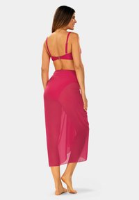 Różowa, przezroczysta narzutka o zwiewnym kroju, z wysokim rozcięciem. Regulowane ramiączka w dopasowanej górze z zapięciem na plecach.