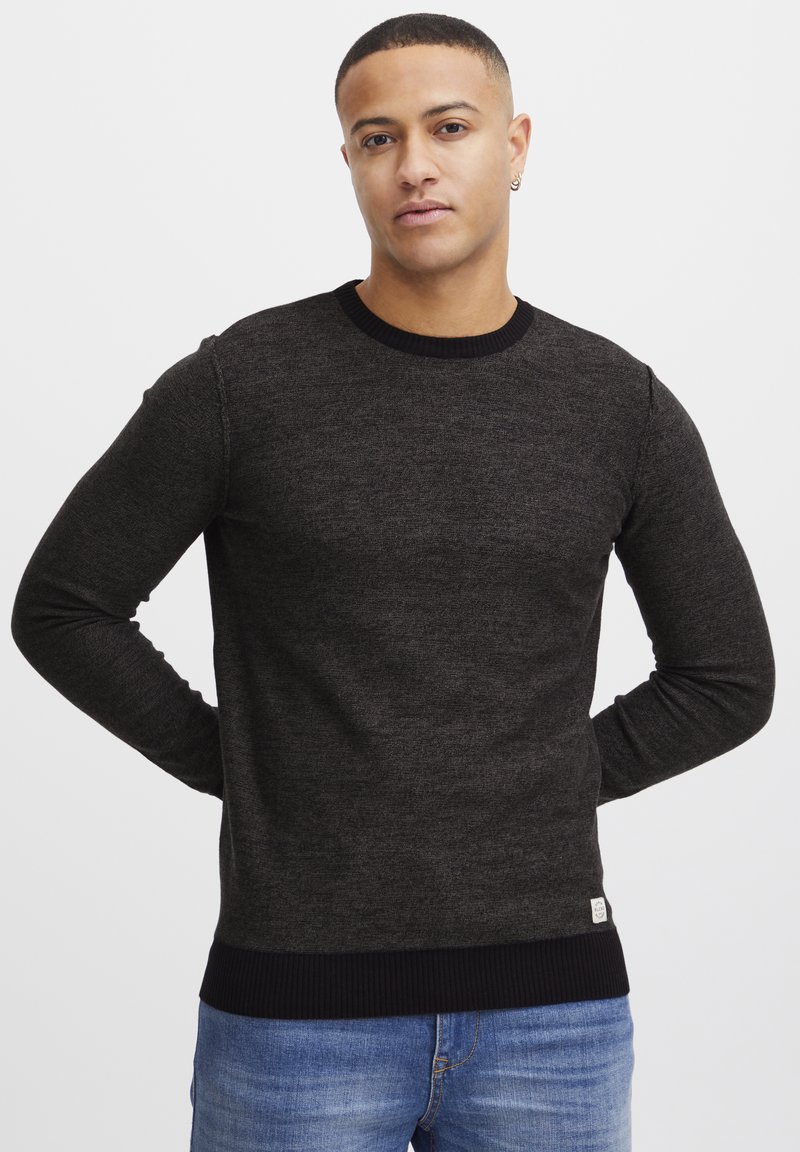 Dunkelgrauer gestrickter Pullover mit langen Ärmeln, Rundhalsausschnitt und gerippten Bündchen. Besitzt ein kleines Etikett am Saum für Details.