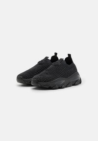 Black slip-on sneakers with a textured upper, featuring a mesh-like design and raised accents. Thick rubber sole for cushioning.
