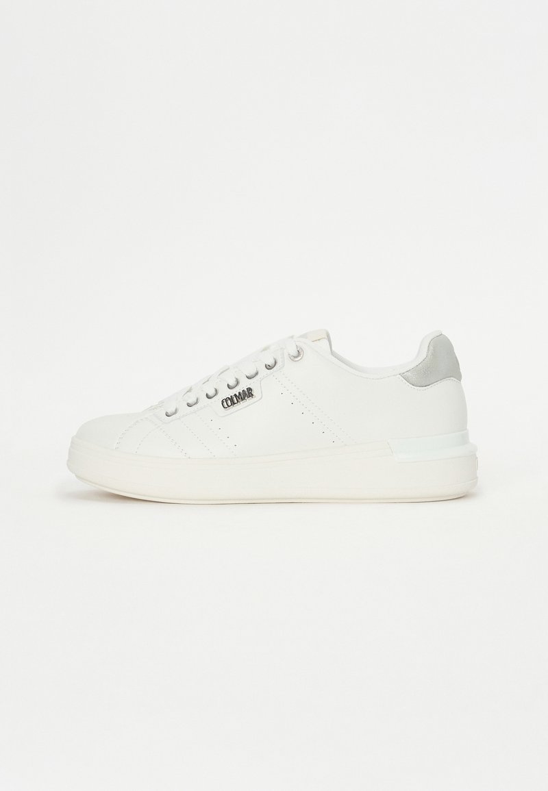 Λευκά δερμάτινα sneakers με διακοσμητικές τρύπες, ασημί λεπτομέρειες στη φτέρνα και χοντρή λευκή σόλα. Οι κορδόνες είναι τοποθετημένες κεντρικά.