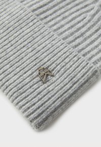 Bonnet en tricot gris avec une texture en côtes et un petit logo métallique en accent. Matériau doux avec un ajustement confortable.