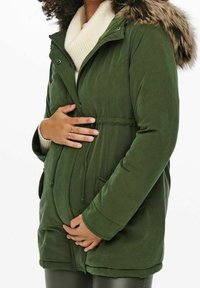 Parka verte avec capuche en fausse fourrure, fermeture éclair, deux poches avant et taille à cordon de serrage. Tissu doux et texturé.