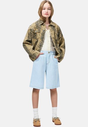 Chaqueta extragrande con estampado de serpiente marrón, blusa crema, pantalones cortos de mezclilla azul claro, calcetines tobilleros blancos y zapatos marrón claro con cordones y superficie texturizada.