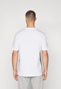 Witte t-shirt met korte mouwen en ronde hals, met zwarte zijstrepen. Gemaakt van katoen met een gladde textuur. Achteraanzicht weergegeven.