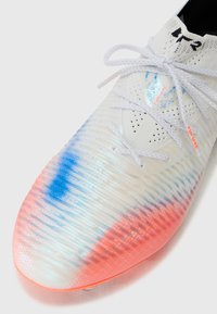 Fußballschuh mit einer strukturierten weißen Oberseite, blauen und pinken Farbverlauf-Akzenten, weißen Schnürsenkeln und Perforationen für Atmungsaktivität.