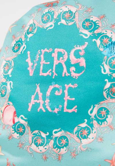 Tissu turquoise arborant le texte "VERSACE" en rose. Entouré d'illustrations ornées sur le thème marin et de motifs étoilés dans des teintes pastel.