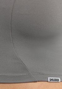 Grauer nahtloser Sport-BH aus dehnbarem Material, mit Flachnähten und einem kleinen Logotag am unteren Rand.