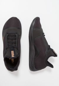 Zapatillas deportivas negras con parte superior de textil suave y suelas de goma. Las características incluyen un cuello acolchado, acentos texturizados y una lengüeta con marca.