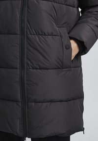 Black puffer jacket with a zip closure, side pockets, and a quilted design. Features a smooth texture and a mid-length cut.