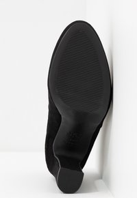 Bottine en daim noir avec une semelle en caoutchouc texturée, dotée d'un talon bas et d'une silhouette lisse et élégante.