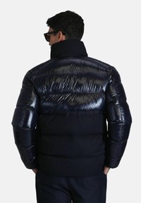 Veste rembourrée bleu marine avec panneaux brillants, col haut, et détails cousus, présentant un design léger et rembourré pour la chaleur.