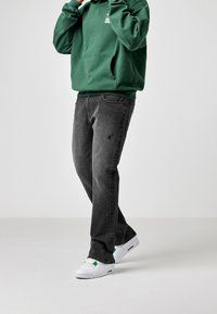 Jeans in denim grigio con una vestibilità rilassata, caratterizzati da zone sbiadite e piccole toppe strappate. Abbinate a una felpa verde e sneaker bianche.