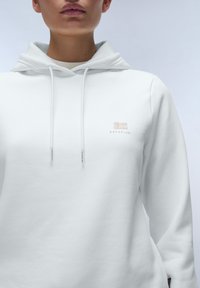 Witte hoodie van zachte stof, met een losse pasvorm, een trekkoordcapuchon en een klein geborduurd logo op de borst.