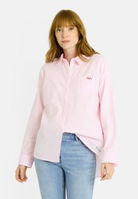 Camisa de botones con rayas rosa claro, mangas largas, un bolsillo en el pecho con el texto rojo "Pale" y un ajuste relajado.