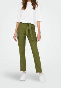 Olijfgroene cargobroek met voorzakken en een strikceintuur, gecombineerd met een losse witte t-shirt en witte sneakers. Gladde stofstructuur.