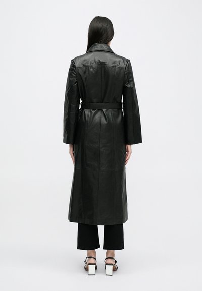 Cappotto trench in pelle nera con una vestibilità su misura, vita cinturata e maniche lunghe. Texture liscia, lunghezza fino al polpaccio e dettagli di cucitura visibili.