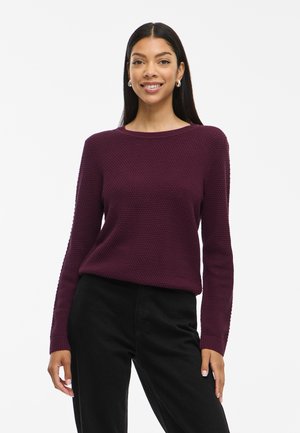 Pull en tricot texturé bordeaux avec un col rond et des manches longues, associé à un pantalon noir, présenté sur un mannequin.