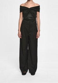 Svart av-axeln topp med rynkad design, ihop med vida svarta byxor. Slät textur och minimalistisk estetik.