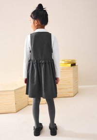 Gray denim dress with a ruffled hem, paired with gray tights and black shoes. White collared shirt is partially visible. Simple design details.