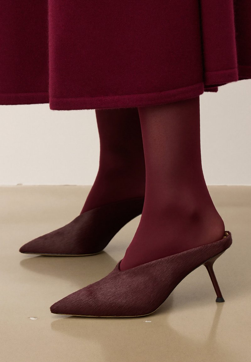 Escarpins burgundy à bout pointu avec une finition texturée, présentant une silhouette élégante et un talon stiletto fin, associés à des collants opaques assortis.