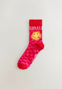 Rot-rosa karierter Socken mit einem gelben Smiley-Gesicht, das X-Augen hat, und dem Text "NIRVANA" in Weiß oben. Aus Baumwollmischung.