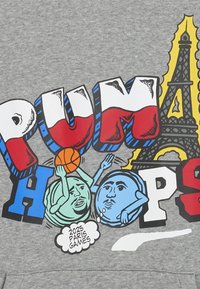 Grijze sweatshirt met gedurfde grafische tekst "PUMA HOOPS," met cartoonachtige bollen die een basketbal vasthouden en de Eiffeltoren op de achtergrond.