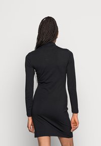 Czarna sukienka z długim rękawem o dopasowanej sylwetce i wysokim kołnierzu. Wykonana z gładkiego, elastycznego materiału, sięgającego do połowy uda.
