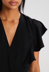 Vestido negro envolvente con mangas cortas y volantes. Confeccionado en una tela suave, presenta un escote profundo y una cintura ajustada.