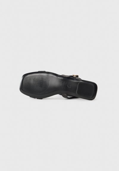 Black heeled sandal with a smooth texture, a rounded toe, and a patterned rubber sole. Features a decorative gold-tone accent.