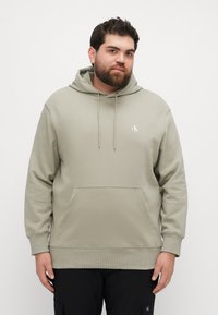 Jasnozielona bluza z kapturem, z kieszenią kangurką, sznurkiem w kapturze i ribbowymi mankietami. Małe białe logo na klatce piersiowej. Miękki, gładki materiał.