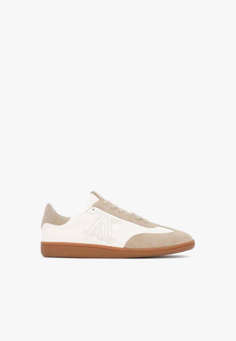 Fehér bőr alapú sneakers, bézs velúrbetétekkel, kerek orral, fűzős elülső résszel és barna gumi talppal. Az oldalon logó található.
