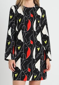 Mekko pitkillä hihoilla mustasta kankaasta, jossa on abstrakti valkoisen, punaisen ja keltaisen kuvio. Suora leikkaus, pyöreä pääntie ja rento istuvuus.