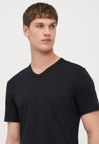 T-shirt noir à col V en tissu doux ; manches courtes, coupe ajustée, design minimal sans logos ni motifs visibles.
