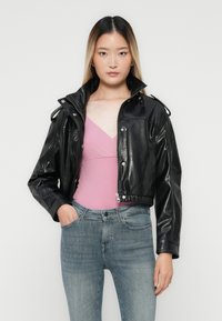 Sort læderjakke med lynlås, skulderlapper og cropped design, parret med en pink top og blå jeans.