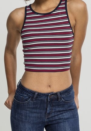 Personne portant un débardeur court sans manches avec des rayures horizontales noires, blanches et rouge foncé, associé à un jean en denim bleu.