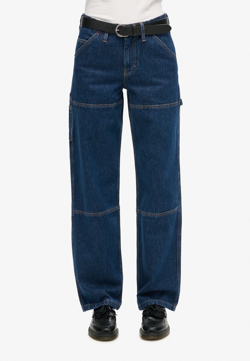 Pantalones cargo de mezclilla azul oscuro con piernas anchas, que presentan múltiples bolsillos, costuras contrastantes y un cinturón negro. Material texturizado y duradero.