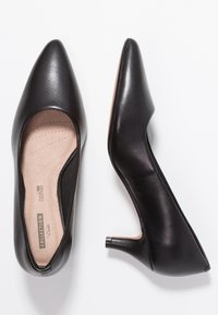Chaussures à talons haut en cuir noir avec un bout pointu, une semelle intérieure rembourrée et un talon bas et élégant. Texture lisse avec une finition polie.
