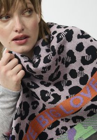 Strickschal mit rosa Grund, schwarzen Leopardenmustern und einem orangefarbenen Band, das "BIG LOVE" in lila Schriftzug trägt.