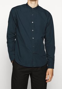 Ciemnoniebieska, długosleeve'owa koszula z kołnierzykiem stojącym, z przodem na guziki i gładką bawełnianą teksturą. Dopasowany krój z zaokrąglonym dołem.